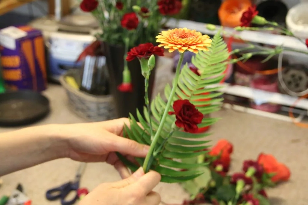 Handbukett med ormbunke och röd blomma